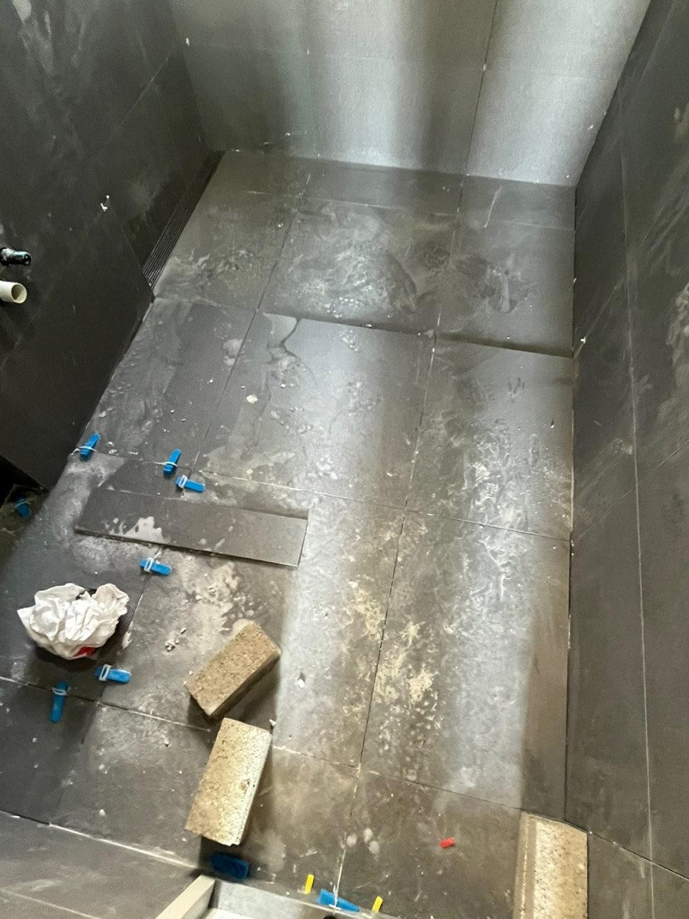 오염물과 배관 부품이 놓인 타일 바닥과 검은색 벽면