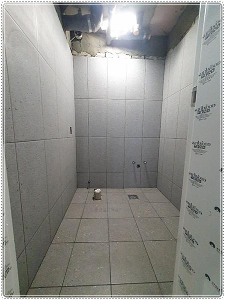 수도꼭지가 노출된 벽면과 배수구가 보이는 타일 시공 단계