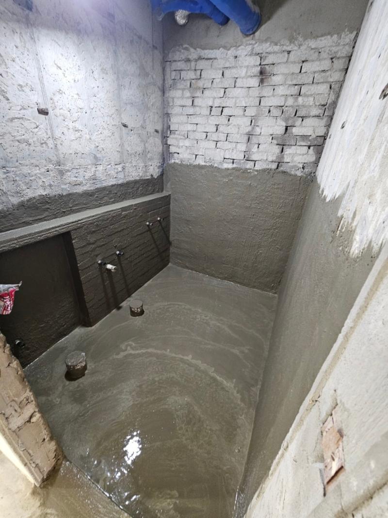 콘크리트 벽과 바닥, 일부 벽면에 브릭이 보이며, 물이 고인 공간. 벽면에는 흰색 코팅과 검은색 부분이 있고, 바닥 중앙에 작은 원통형 구조물이 두 개 있다.