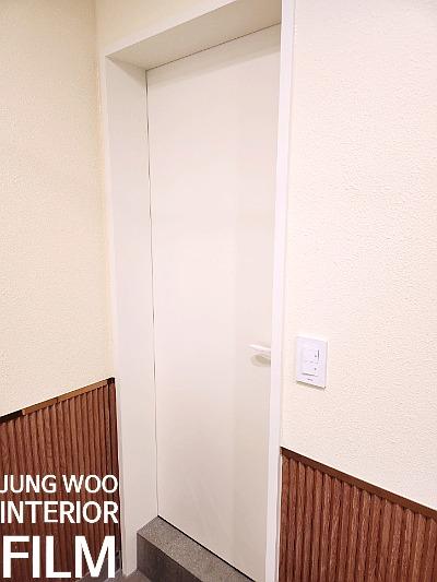 나무 패널 하단 벽면과 흰색 도어가 설치된 현관