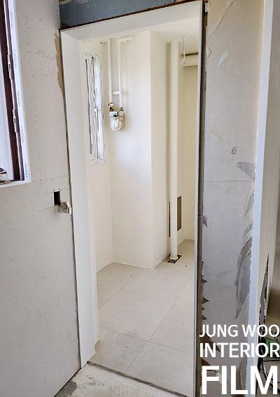 배관이 설치된 벽면과 문틀 마감 작업 중인 복도