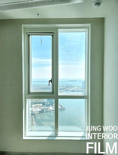 실내 벽면과 창호가 보이는 창호 근접 샷. 창호는 4분할 구조로, 상단 좌측 창호는 열림 상태로 끈이 매달려 있고, 외부 풍경은 하늘과 물, 도시 풍경이 보임.