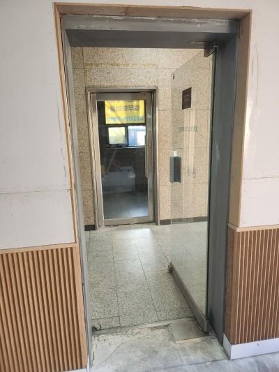 나무 패널과 흰색 벽지가 적용된 엘리베이터 앞 복도