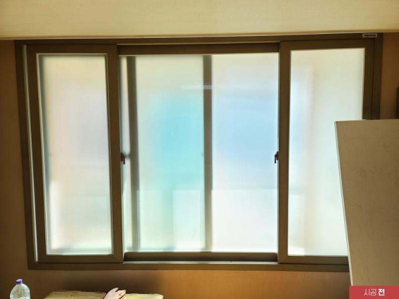 창호의 유리 패널과 프레임이 보이는 창호 근접샷. 창호는 3개의 패널로 구성되어 있으며, 중앙 패널은 투명 유리로 빛이 들어오고 양쪽 패널은 흐릿한 유리로 처리되어 있다. 창호 프레임은 갈색 계열로, 창호 아래쪽 벽