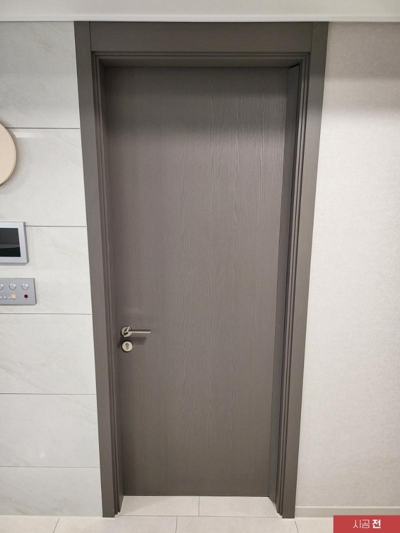 현관 벽면과 대비되는 회색 목재 질감의 도어