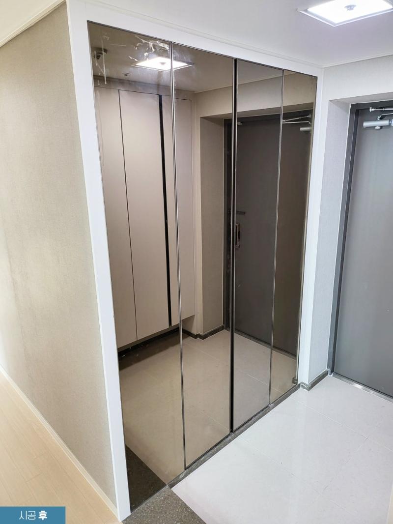 유리 문으로 된 수납장이 있는 복도 공간. 벽은 베이지색 벽지로 마감, 바닥은 밝은 색 타일로 되어 있으며, 천장에 스퀘어 형 조명이 설치됨.