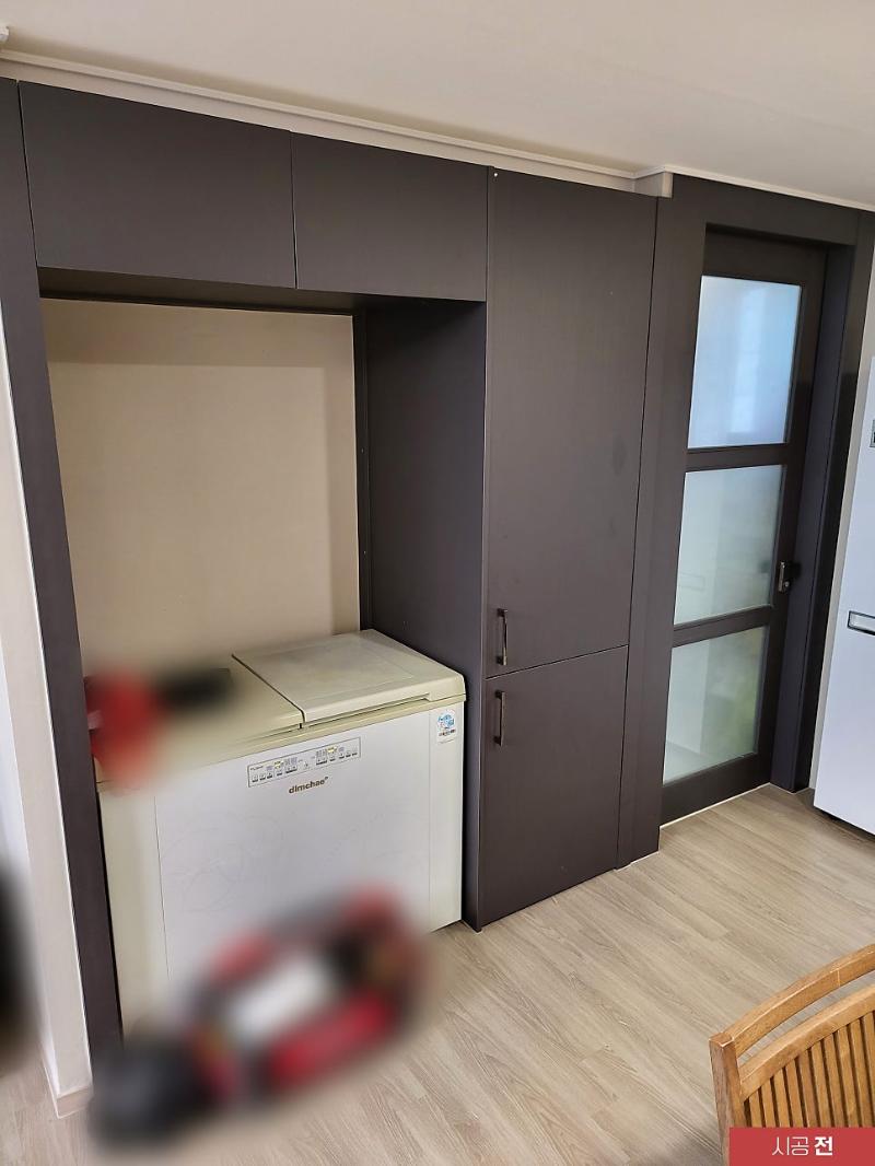 실내 공간에 검은색 수납장, 흰색 냉장고, 유리문이 있는 벽면, 목재 바닥이 보임