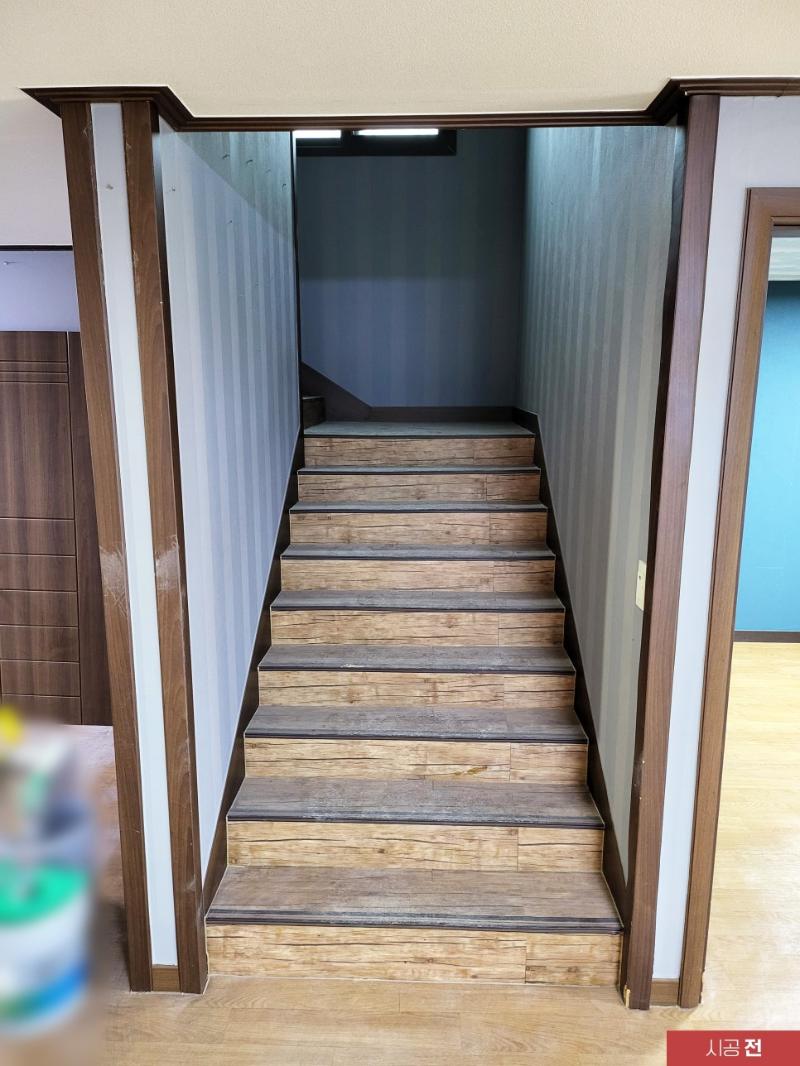 목재 계단과 줄무늬 벽지가 보이는 시공 전 복도