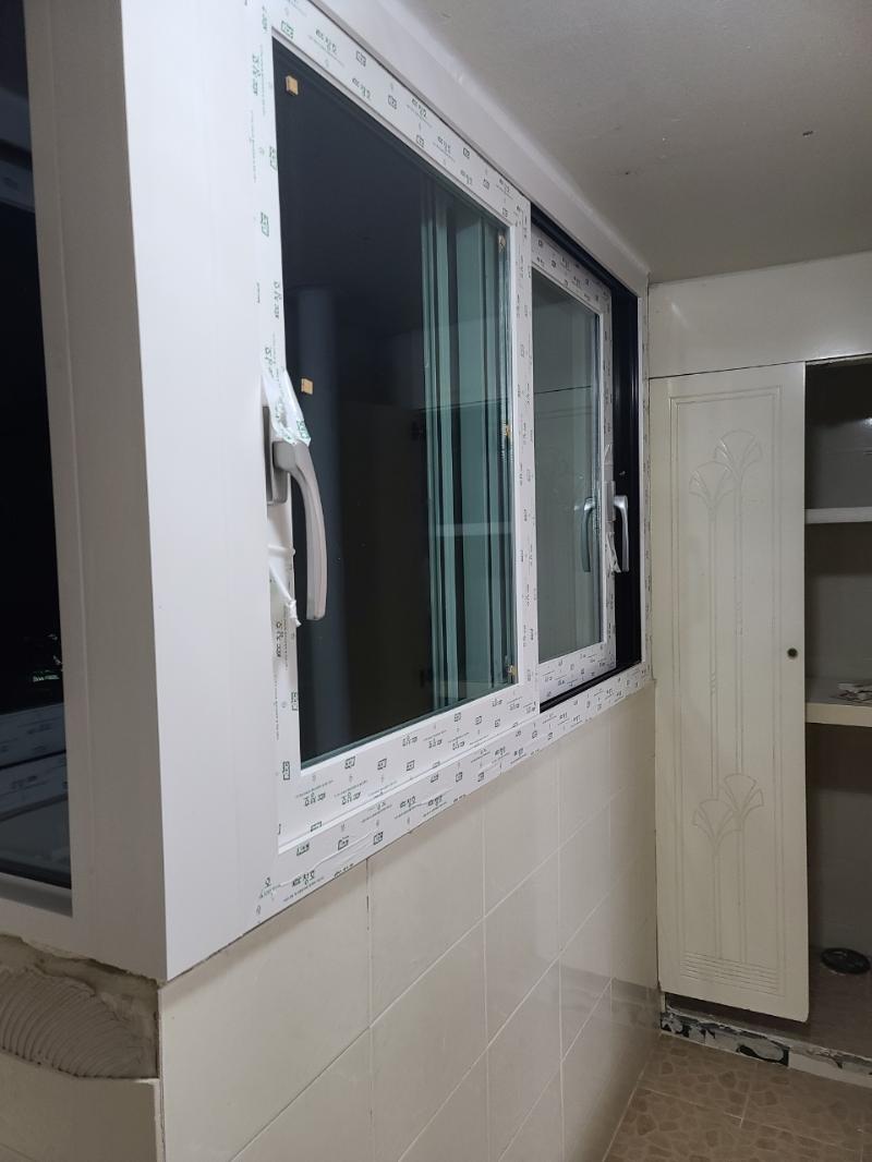 베이지색 타일 벽면과 흰색 보호 필름이 붙은 창호 프레임