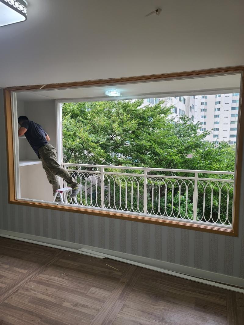 도배된 벽면과 목재 마루가 있는 실내 창가 작업 모습